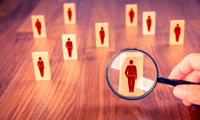 Multiple different wooden figures with red people drawn on with a magnifying glass over one figure