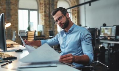 bearded engineer in eyeglasses and formal wear looking at blueprint while working in the office