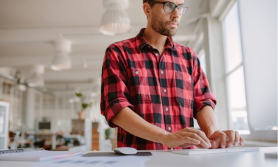 Shot of young man standing at his desk and working on computer