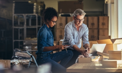 Man packing his product in the box while his business partner prepares the invoice