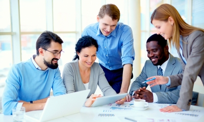 A group of office workers stand around a table looking at a computer