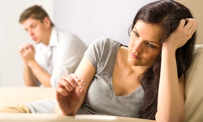 Divorce and family law Sad young woman sits looking at her wedding ring with man in the background
