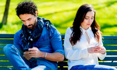 A couple sat down on a bench looking at their mobiles