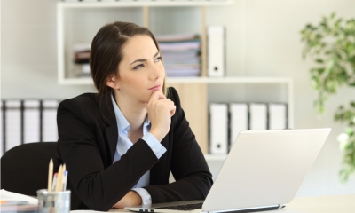 Woman in a suit sat at a desk with a laptop thinking about a career reboot