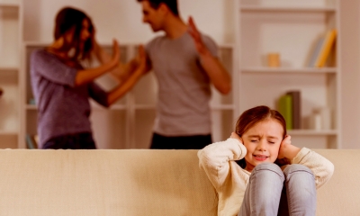 Small girl covering her ears with a couple having a domestic argument in the background