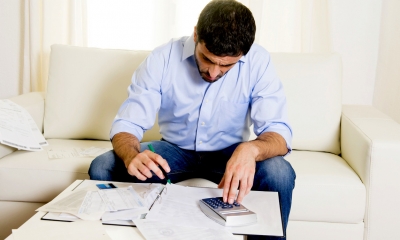 Man in a blue shirt sat on a sofa using a calculator to work out the cost of a divorce