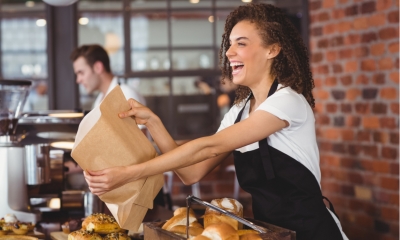 Laughing barista giving paper bag to customer at coffee shop