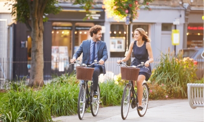 Businesswoman And Businessman Riding Bike Through City Park