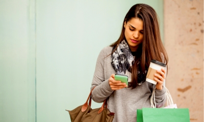 Young woman using her smartphone and drinking coffee while doing some shopping in a mall Young woman using her smartphone and drinking coffee while doing some shopping in a mall