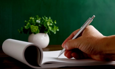 Close up of a hand writing on a probate document with a green plant in the distance