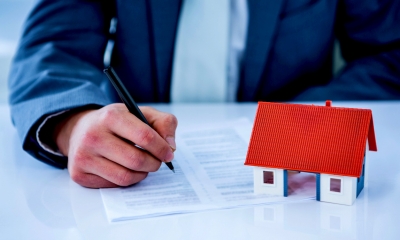 Man in suit writing on a piece of paper with a toy house next to it