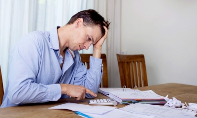 Stressed man in a blue shirt working out his financial settlement with a calculator for his divorce