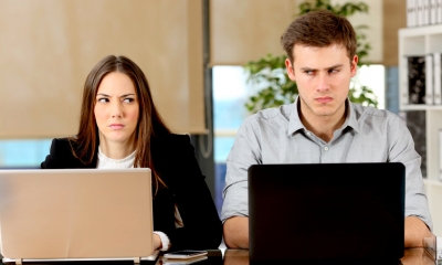 Man and a woman glaring at each other whilst using their laptops