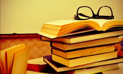 Pile of books with a pair of glasses resting on an open book at the top of the pile