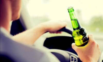 Man sits at steering will of car holding bottle of beer