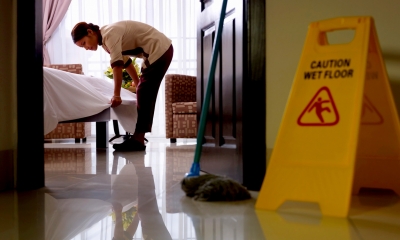 Yellow 'caution wet floor' sign with worker cleaning in the background