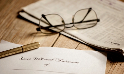 Wooden tabletop with glasses lying on a newspaper and pen lying on a paper with Last Will and Testament written on it