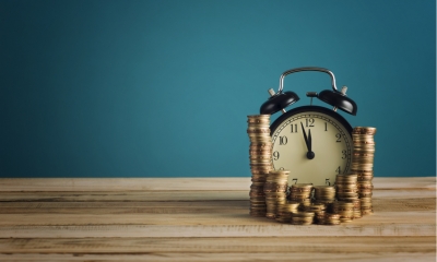 Coins stacked up around an alarm clock on a wooden table