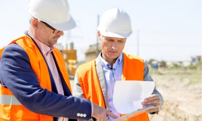 Engineers examining documents on clipboard at construction site against clear sky Engineers examining documents on clipboard at construction site against clear sky