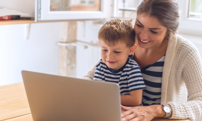A young mum helps her primary-aged son do his classwork online