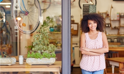 Young mixed race woman smiling while standing in the door of her cafe with her arms folded proud to be the owner of a small business